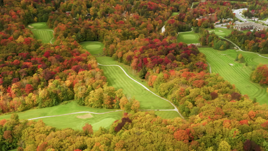Cinematic bright green golf field at Killington Mountain resort with scenic fall foliage forest landscape background on sunny autumn day. 4K aerial Killington golf course on sunny colorful fall day
