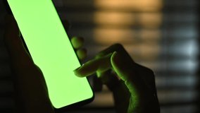 Close-up of female hands using smartphone with mock up green screen chroma key at night. Girl scrolls the phone, browsing social networks, news, surfing the Internet, online shopping. Video template