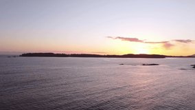 A drone video of the ocean during sunset with an island in the distance.