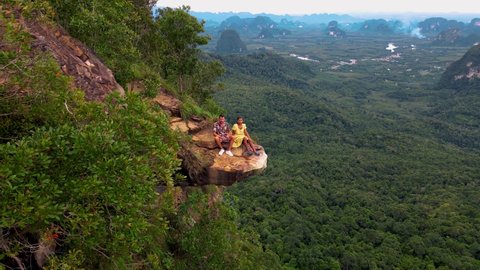 Dragon Crest mountain Krabi Thailand, a Young traveler sits on a rock that overhangs the abyss, with a beautiful landscape. Dragon Crest or Khuan Sai at Khao Ngon Nak Nature Trail in Krabi, Thailand