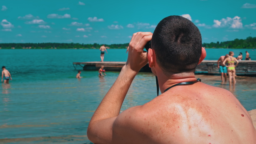 Man on the beach in swimming trunks is watching someone through binoculars. The lifeguard on the beach keeps order in the water. Curious man looks through binoculars at nature. maritime emergency | Shutterstock HD Video #1091582989