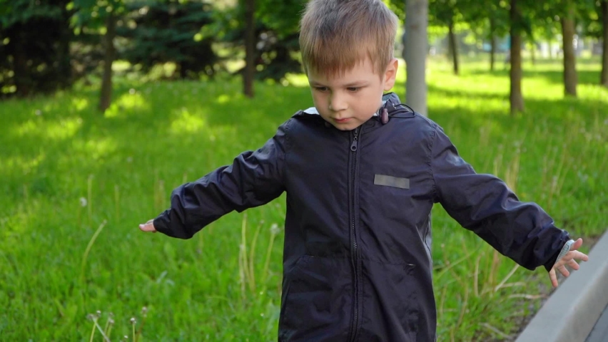 The boy walks along the curb and keeps his balance