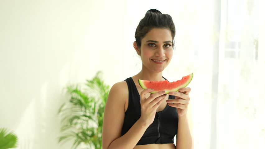 A Indian Beautiful young woman eating a slice of watermelon and smiling after yoga. Summer and lifestyle concepts.closeup camera.good health.female fitness. 
