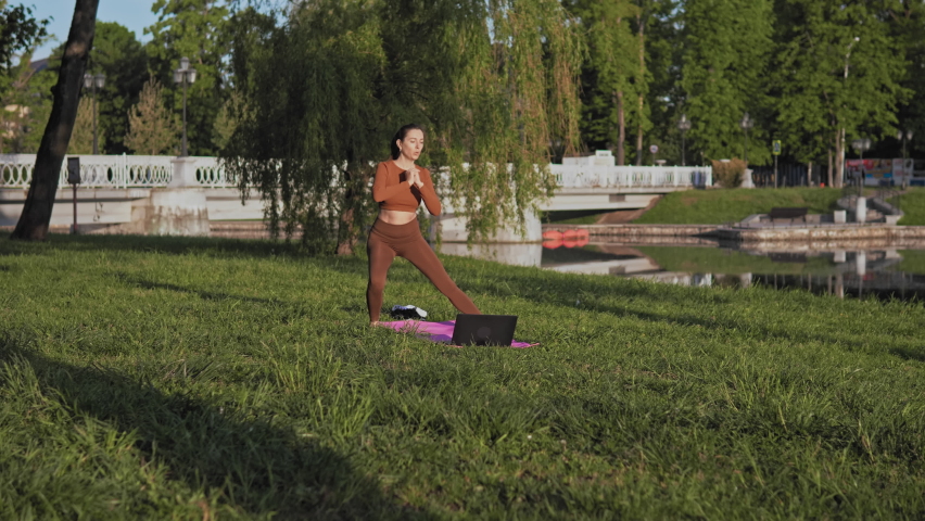 Medium shot of young caucasian woman standing on a pink yoga mat and doing stretching exercises in public park at early morning. Concept of healthy lifestyle. Caucasian female dressed in sports | Shutterstock HD Video #1091589881