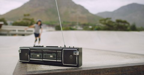 Closeup of a retro radio panning to cool urban skaters practicing their skills. Young fun female rollerbladers playing a cassette player in a skate park outside. Girls listening to music on a boombox