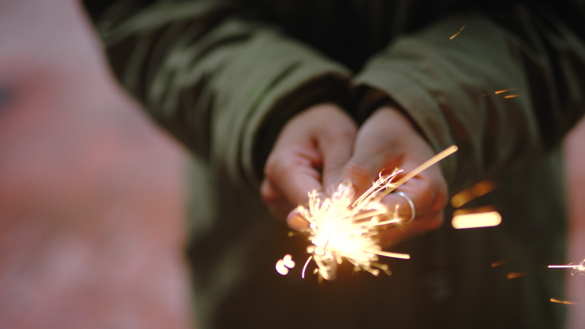 Closeup of womans hands holding a sparkler and standing alone outside. One playful woman holding a lit bengal light and celebrating an event. Playing with sparkles or sparkly fireworks and having fun | Shutterstock HD Video #1091593285