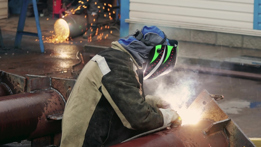 View of welder near pipe at work. Video 4k resolution. Welder in protective mask welds pipe and sparks fly. Industrial construction. Real workflow. Royalty-Free Stock Footage #1091594975