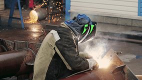 View of welder near pipe at work. Video 4k resolution. Welder in protective mask welds pipe and sparks fly. Industrial construction. Real workflow.