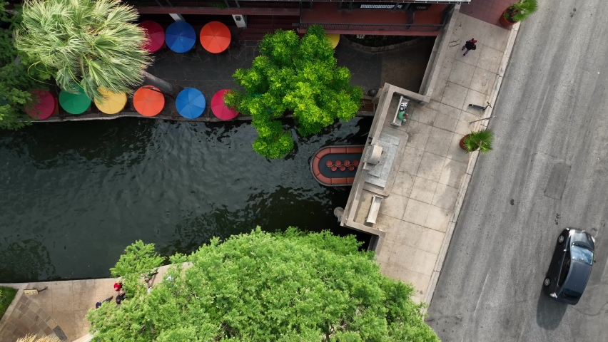 Boat navigates river in downtown urban San Antonio TX. Texas River Walk is top famous tourist attraction in city. Aerial view. Colorful umbrellas at outdoor restaurant.