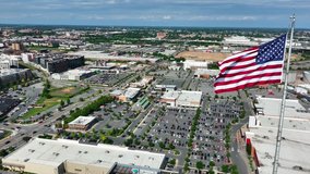 American flag proudly flies over urban city in USA. Retail shopping mall, office building, homes and houses. Aerial orbit. - Powered by Shutterstock - Get 15% off with code: PIKWIZARD15