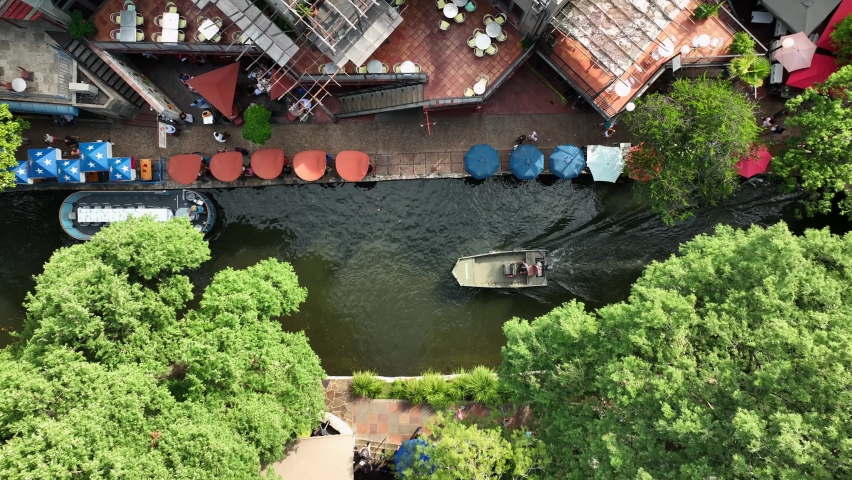 San Antonio TX famous River Walk. Aerial top down birds eye view of boats and barges passing by city restaurants in downtown.