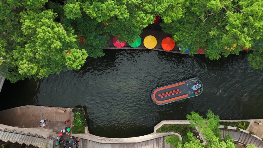 Small boat passes under bridge beside San Antonio River Walk. Famous tourist attraction. Aerial.