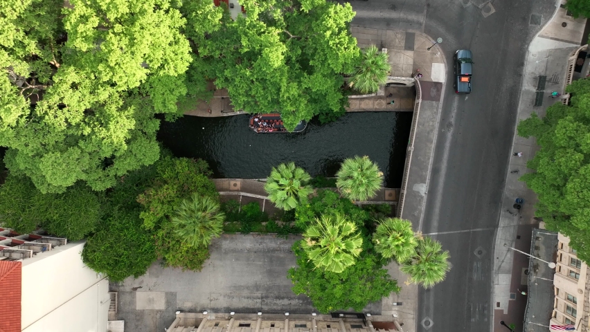 San Pedro Creek and Arneson River flow through downtown San Antonio River Walk park. Barge full of tourists. Descending aerial.