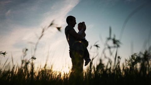 father and son silhouette. happy family kid dream concept. father holding in his arms in the grass in nature at sunset shadow silhouette. fathers day. father and son in the park sunset silhouette Arkivvideo
