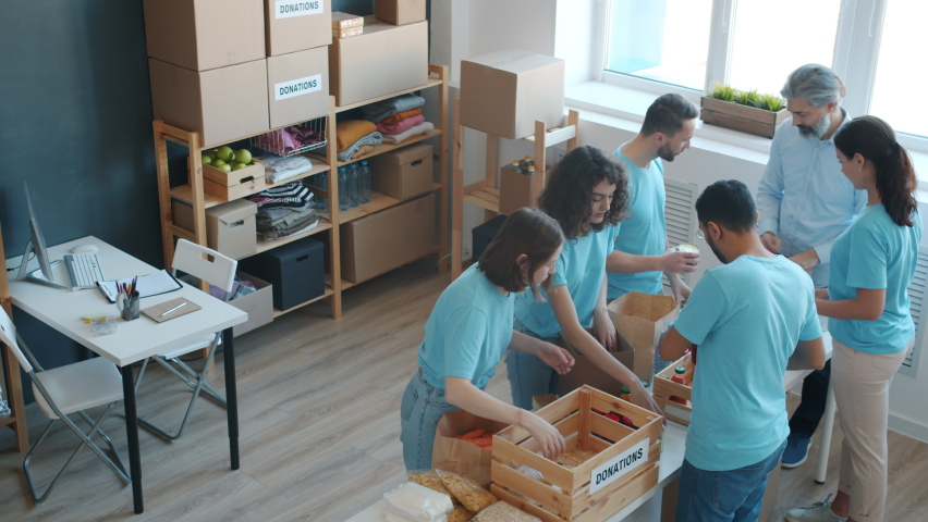 Diverse group of enthusiastic volunteers packing donation boxes with food and talking in charity fund office. Teamwork and humanitarian aid concept. Royalty-Free Stock Footage #1091600169