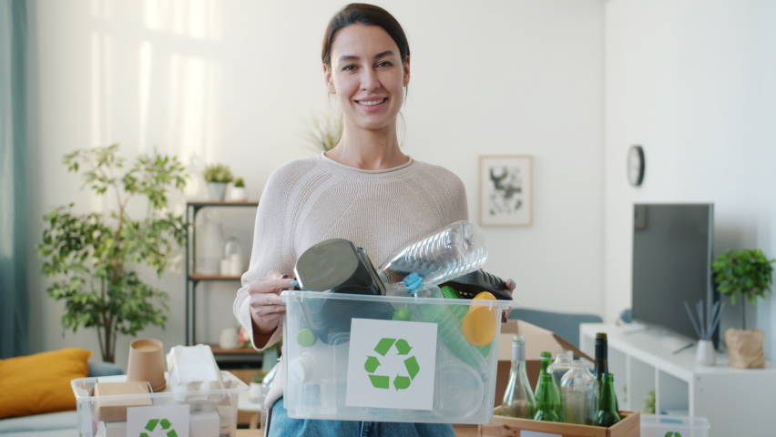 Smiling young lady holding container with plastic for recycling standing indoors at home and looking at camera. People and ecology concept. | Shutterstock HD Video #1091600207