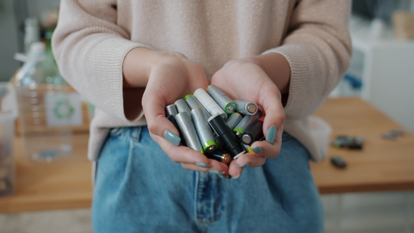 Close-up of female hands holding batteries with recycling boxes visible in background in apartment. Ecological problems and zero waste concept. Royalty-Free Stock Footage #1091600257