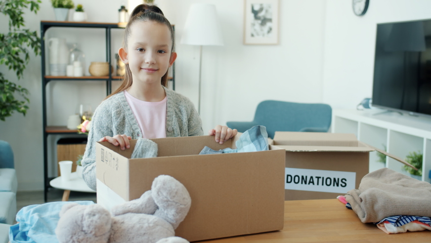 Slow motion portrait of beautiful child standing in nursery room with donation box filled with toys and clothes smiling and looking at camera | Shutterstock HD Video #1091600259
