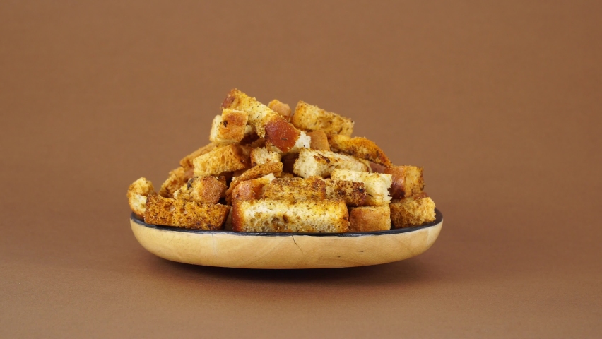 Handmade white bread croutons cubes on brown background rotates. Food background. Bread , homemade croutons with garlic rotates in wooden plate rotating on white. Homemade croutons in wooden bowl.