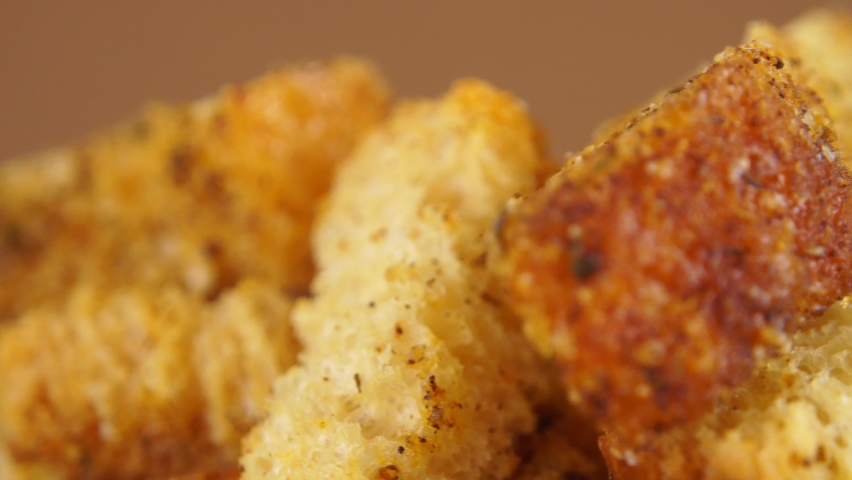 Crispy bread cubes, extremely macro view, crouton or brown roasted tostes rotating on brown. Crouton or roasted crackers cubes rotating in wooden plate. Mock up image of homemade croutons in a bowl.