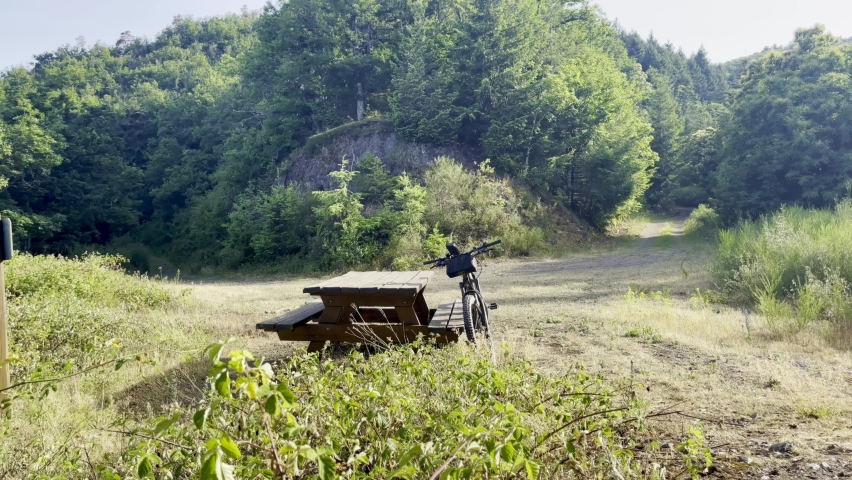 MTB bike leaning against a picnic table near a mountain sloping hairpin path in the Florival valley