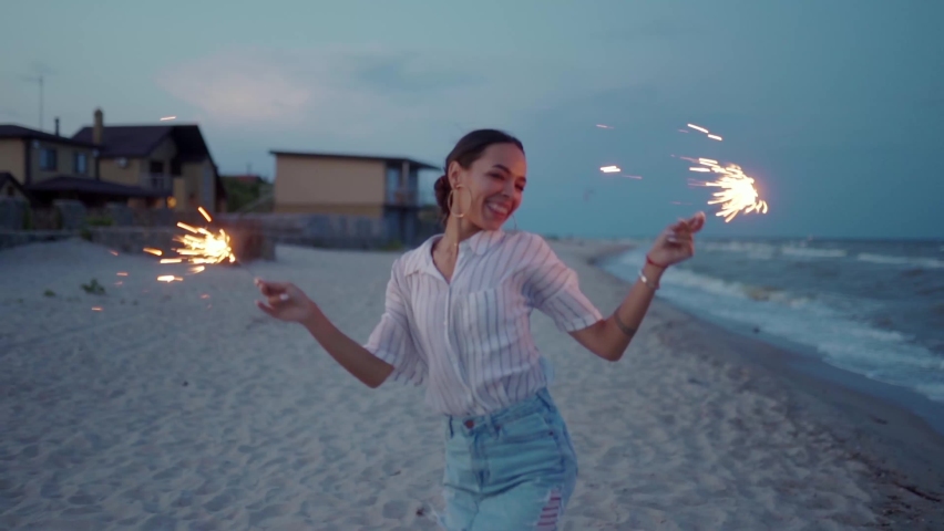 African american woman walking, dancing, having fun on night party at seaside with sparklers lights in hands on Fourth of July. Pretty girl partying on beach with fireworks on New Year, Christmas. | Shutterstock HD Video #1091602453