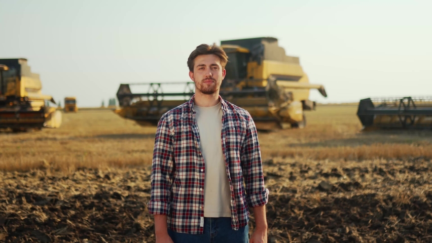 Portrait of proud farmer crossing hands on chest in harvested wheat field. Harvester machine driver standing at his combine. Smiling agronomist looking at camera. Rancher at harvesting work. | Shutterstock HD Video #1091602501