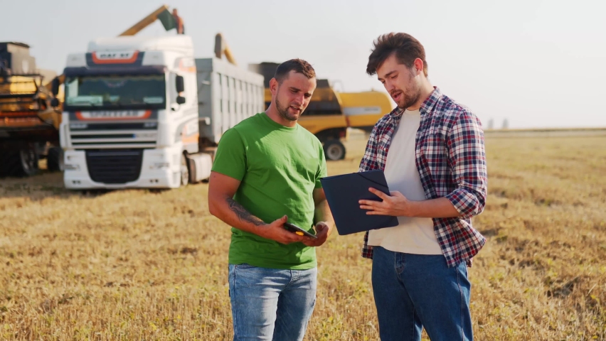 Farmer, logistics agent sign agreement on grain supply, shake hands in wheat field. Agronomist discuss agriculture business contract. Rancher, landlord negotiate with handshake. Harvesters load truck. Royalty-Free Stock Footage #1091602507