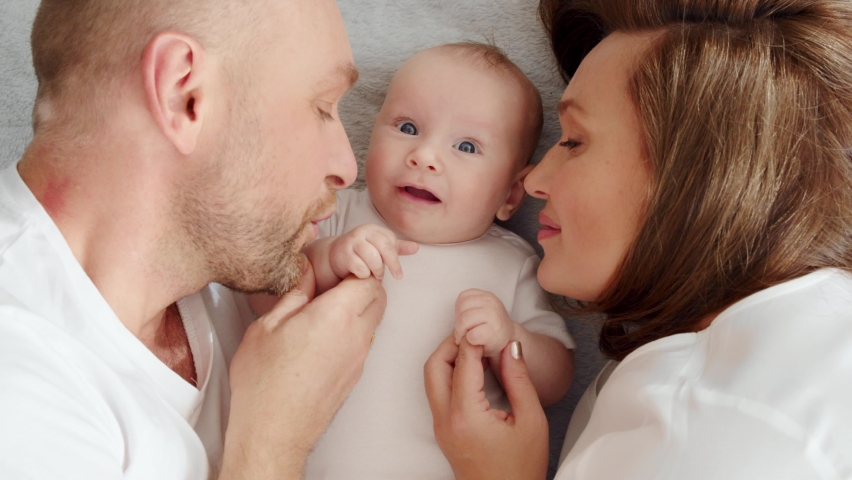 Newborn baby with happy parents, top view. Happy family.  Healthy newborn baby in a white t-shirt with mom and dad. Close up Faces of the mother, father and infant baby.  Cute  Infant boy and parents