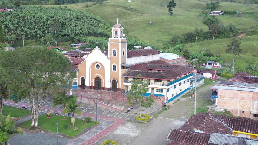 Small traditional village - town in Antioquia Colombia near Andes surrounded by nature, with colorful facades, church in park, small park, clay tiles roofs, cobblestone streets. Drone 4K.