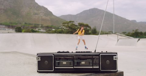 Female roller skater dancing in a city skate park outside, spinning and having fun. A boombox panning to cool urban skater full of energy practicing skills and listening to music on a radio