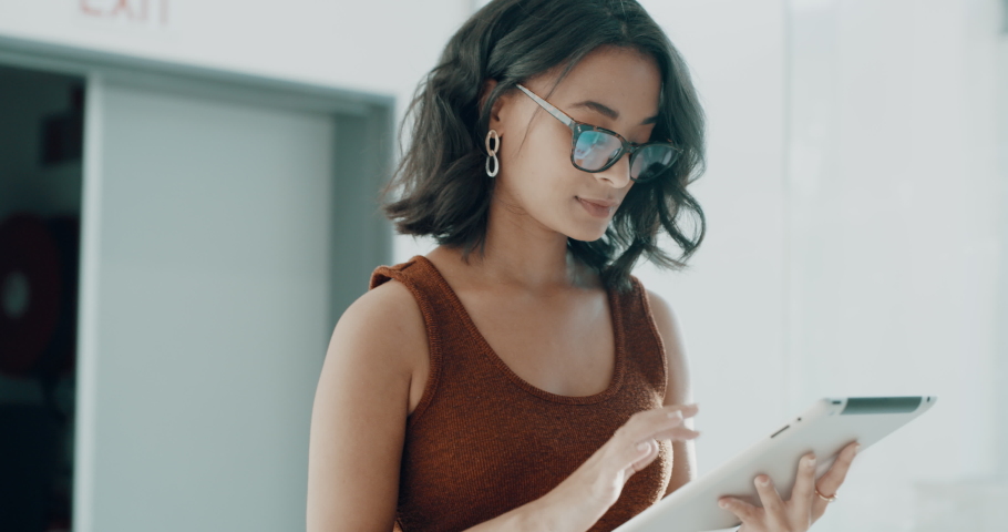 Powerful Latin businesswoman using a digital tablet while walking in an office at work. A young female entrepreneur wearing glasses walking and using wireless technology in a startup business | Shutterstock HD Video #1091604771