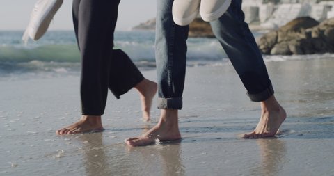 Closeup on feet of free young couple walking barefoot on sandy beach and enjoying fresh air together on vacation. Husband and wife taking a slow, romantic walk at sunset while getting their toes wet
