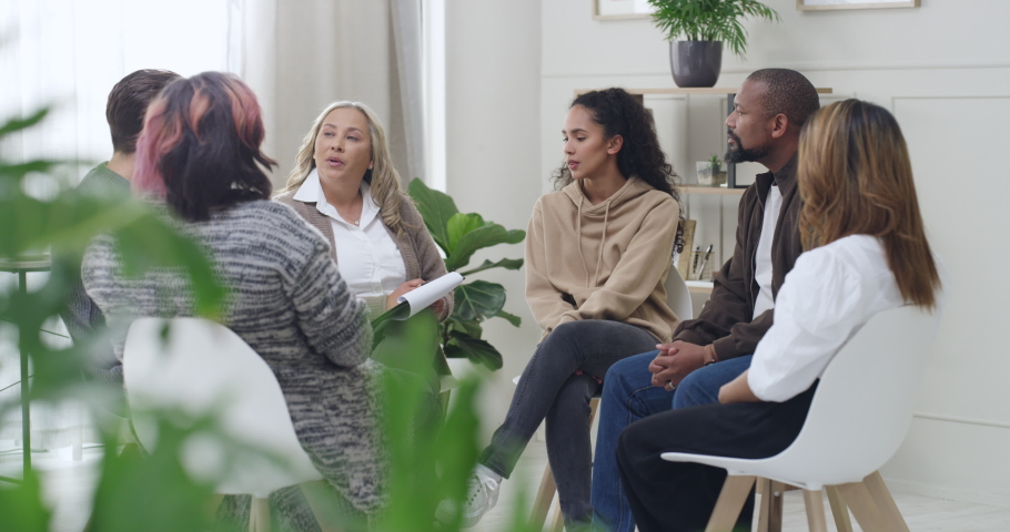 Diverse support group during a meeting with a professional mature female therapist. Group of employees looking serious during a team counselling session. Mental health in the professional workplace | Shutterstock HD Video #1091605085