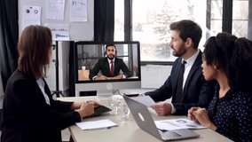 Cooperation, teamwork concept. Group of successful business people of different nationalities, sitting in modern office, brainstorming together, talking with their colleague, boss by video conference