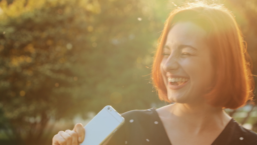 Attractive teen redhead girl active carefree woman listens music on mobile phone sound app dancing moves rhythmically in sunlight sunset singing favorite song at smartphone like microphone enjoys life | Shutterstock HD Video #1091609307