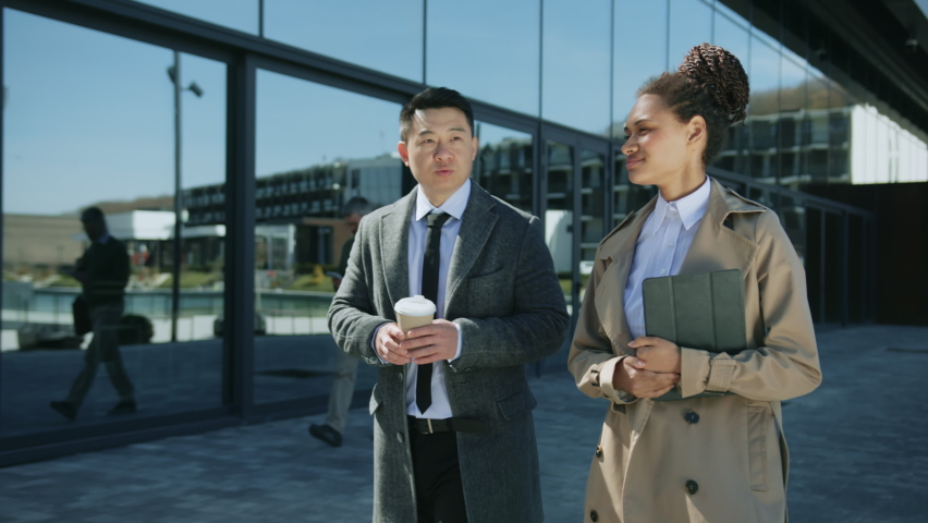 Two young business people walking talking spend time together outside. Drinking coffee smiling. Sunlight. Slow motion