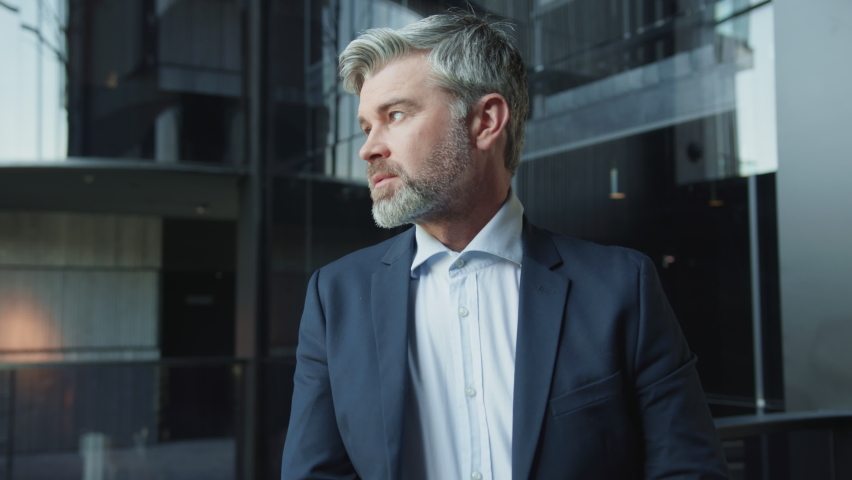 Portrait of serious gorgeous middle-aged businessman looking straight at camera in modern office. Close-up footage of handsome bearded gray-haired man in suit. Lifestyle, boss. Confident Caucasian Royalty-Free Stock Footage #1091609551