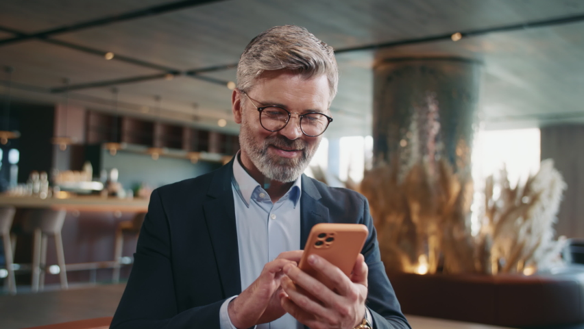 Portrait of good-looking thoughtful middle-aged Caucasian man looking away, writing message. Smiling Caucasian restaurateur chatting, using smartphone while sitting on couch in comfortable restaurant Royalty-Free Stock Footage #1091609571