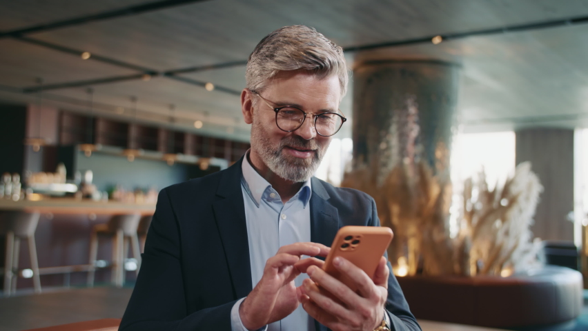 Portrait of good-looking thoughtful middle-aged Caucasian man looking away, writing message. Smiling Caucasian restaurateur chatting, using smartphone while sitting on couch in comfortable restaurant Royalty-Free Stock Footage #1091609571