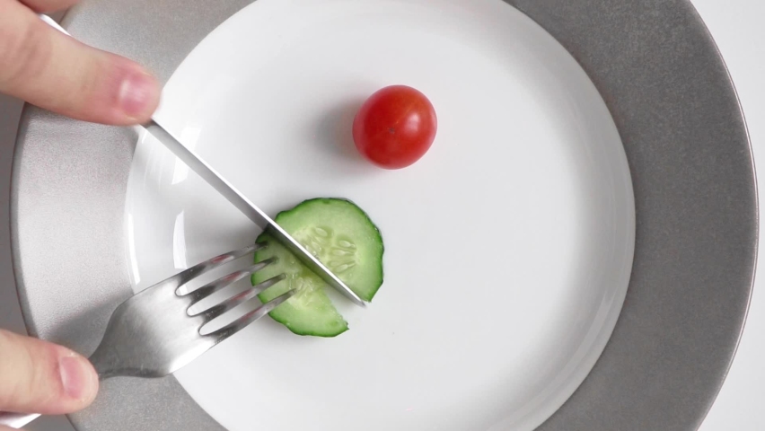 Vertical Video Man on diet eats little chili tomato and cucumber from plate. Concept slimming and healthy food. Natural ingredients. Vegetables and healthy eating. Portion control No animal byproducts