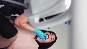 Vertical Video Professional Woman Dentist in Medical Gloves with an Assistant Examines Female Patient in Dental Clinic. Dental Treatment and Care. Modern Dentistry. Concept of Healthcare and Medicine