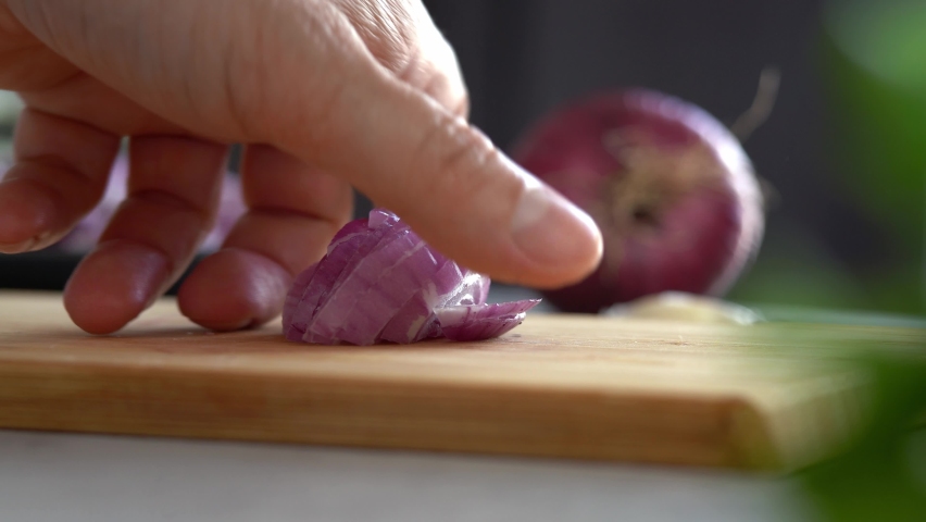 Close up of male hands cut fresh red onion on wooden cutting board on background of vegetables and greens in kitchen. Chop. Cooking food. Royalty-Free Stock Footage #1091613083