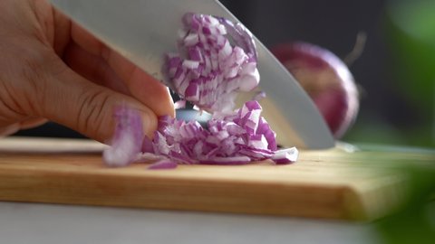 Стоковое видео: Close up of male hands cut fresh red onion on wooden cutting board on background of vegetables and greens in kitchen. Chop. Cooking food.