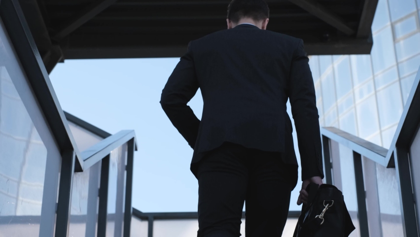 Businessman with a briefcase in his hands climbs the stairs, rear view. The man goes to the office