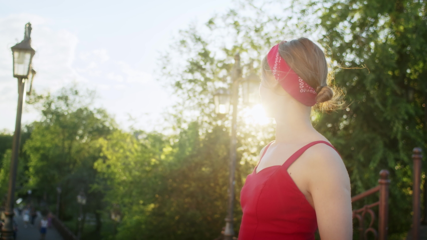 Happy girl in red dress walking in the park, enjoying the setting sun on the street, summer lifestyle. | Shutterstock HD Video #1091616335