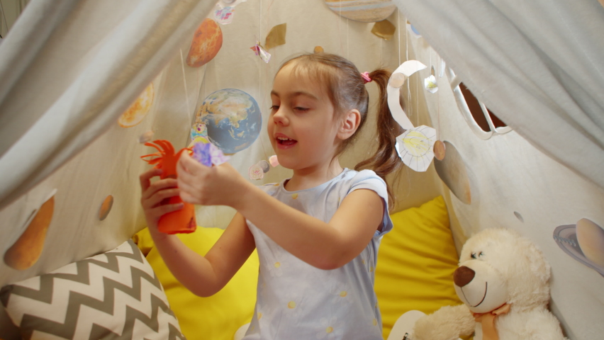 Cute little girl plays space aliens by launching them through the planets. Imagination Fly and play aliens from outer space. Childish dreamy lifestyle of a little aviator in the room.  | Shutterstock HD Video #1091616387