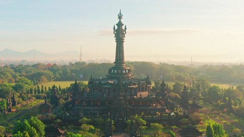 Amazing aerial view on Bali temple Bajra Sandhi monument in Denpasar in the rays of the rising sun against the backdrop of picturesque mountains on the horizon. Bali, Indonesia 4K Aerial view