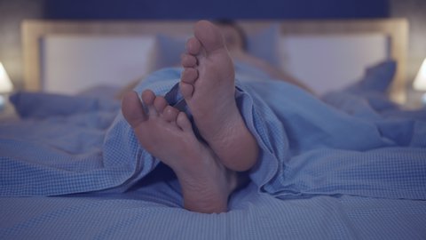 Bare feet of a man from under a blanket, lying in the bedroom on the bed, close up