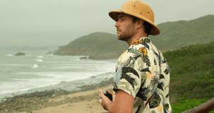 Lifestyle young man blogger working on the beautiful beach, freelance travel on holiday summer, blue sky outdoors. Summer Vacation Concept. stylish blogger traveler in a safari hat takes a photo